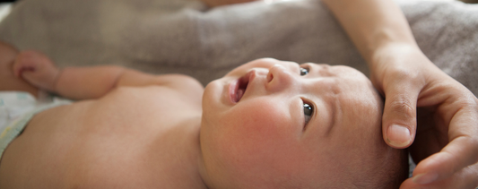 Baby looking up at its parent. Parent's hand on babies forehead